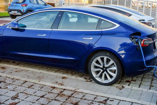Cremona, Itally - October 6th 2024 Deep blue metallic tesla model 3 long range with dual motor all-wheel drive charging its battery at a charging station