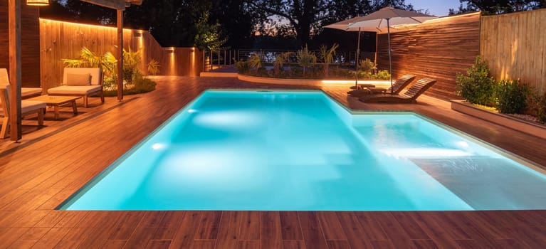 A luxurious poolside with glowing lights, comfortable loungers, and garden surroundings, creating a serene evening ambiance. Concept of peaceful relaxation and elegant outdoor living at night