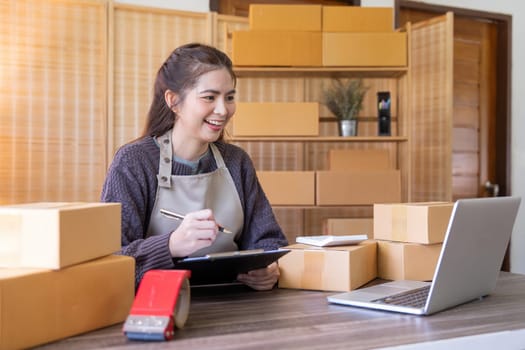 Young woman working online ecommerce shopping at her shop. Young woman seller prepare parcel box of product for deliver to customer. Online selling, ecommerce. Selling products online.