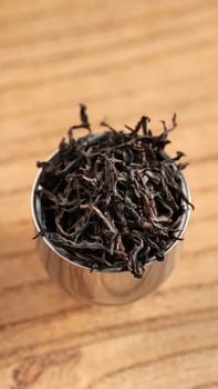 A closeup view of dried black tea leaves being held in a metal scoop placed on a rustic wooden background