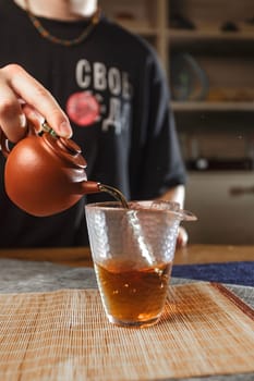 A closeup of tea being poured from a crafted teapot into a delicate glass cup, showcasing a cozy tea moment