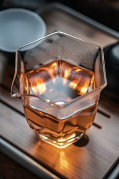 A stylish hexagonal glass teacup showcasing warm tea tones along with beautiful reflections on a wooden surface