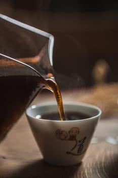 This is a closeup image of rich coffee being poured from a stylish pitcher into a steaming hot cup