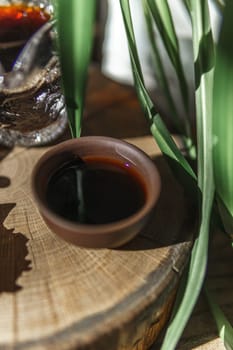 A beautiful view shows dark syrup in a clay bowl, surrounded by greenery and textures, creating a captivating scene