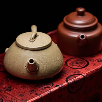Two stunning and beautiful Chinese tea pots are displayed elegantly upon a rich and vibrant red fabric beneath them