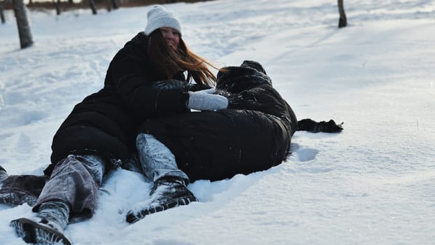Two young girls having fun during their winter vacation, playfully tussling in the snow while wrapped up in cozy winter attire