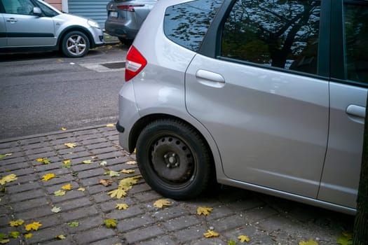 Lombardy, Italy - November 20th 2024 Parked silver honda jazz hybrid on a cobblestone street with fallen autumn leaves
