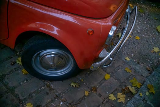 Lombardy, Italy - November 20th 2024 Close-up of a vintage red fiat 500 parked on a cobblestone street, adorned with fallen autumn leaves