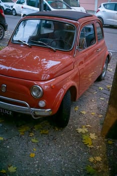 Lombardy, Italy - November 20th 2024 Classic red fiat 500 parked on the side of a street, with fallen autumn leaves scattered on the ground