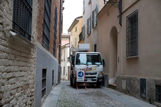 Lombardy, Italy - November 20th 2024 White mitsubishi fuso canter truck with an aerial work platform parked in narrow european cobblestone street between old buildings