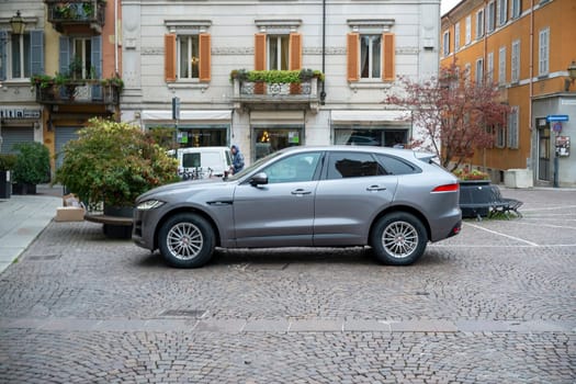 Lombardy, Italy - November 20th 2024 A grey jaguar f-pace suv is parked on a cobblestone street in a picturesque european city, showcasing luxury and urban lifestyle