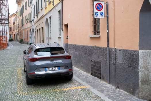 Lombardy, Italy - November 20th 2024 Rear view of a grey cupra formentor parked in a no parking or stopping area reserved for disabled people in a narrow cobblestone street of an italian town