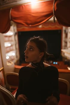 In a theater setting, a young woman gazes thoughtfully, capturing a beautifully nuanced moment of intrigue and elegance