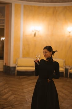 A stylish woman dressed in a beautiful black dress elegantly poses with a glass in a classic vintage interior setting