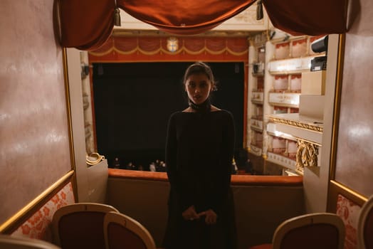 A poised figure elegantly stands in a grand theatre box, surrounded by a stunning interior, ready for the show