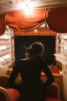A woman in a stunning black dress intently gazes at the stage from comfortable theater seats, lost in thought