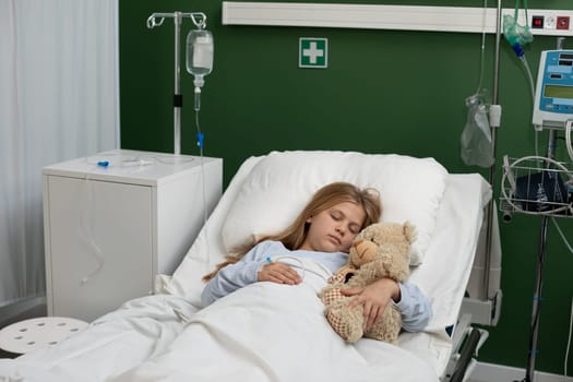A girl rests in a cozy hospital bed, comforted by her teddy bear, showcasing love, care, and warmth