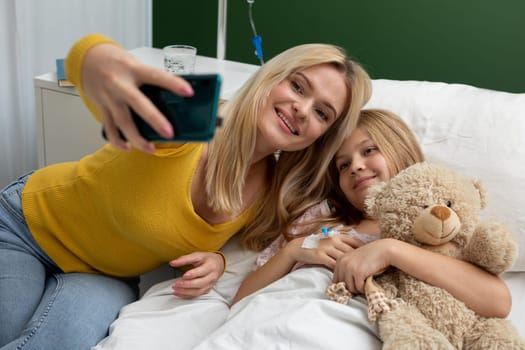 A loving mother and her daughter joyfully share a cheerful moment as they take a delightful selfie in a hospital room