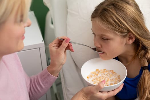 A loving mother helps her daughter eat cereal, showcasing care and support in a nurturing environment.