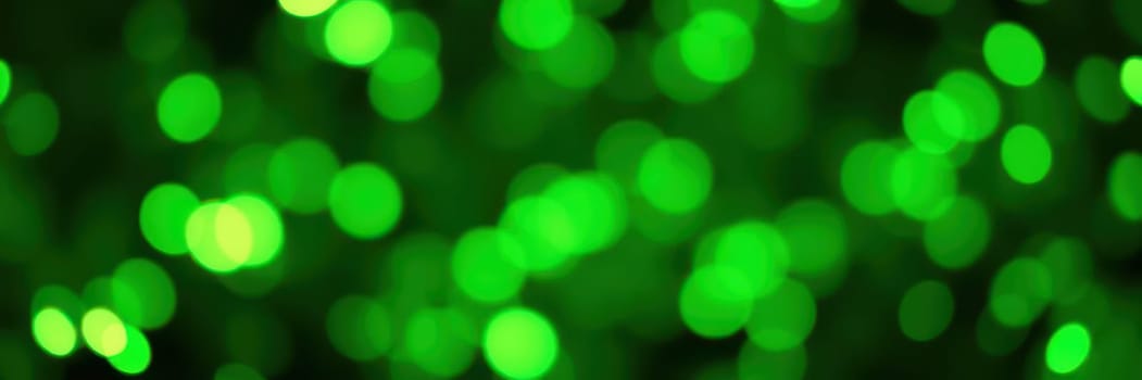 Colorful bokeh lights twinkle in various shades of green, illuminating a lively outdoor gathering in a city park during the evening. The ambiance feels joyful and celebratory.