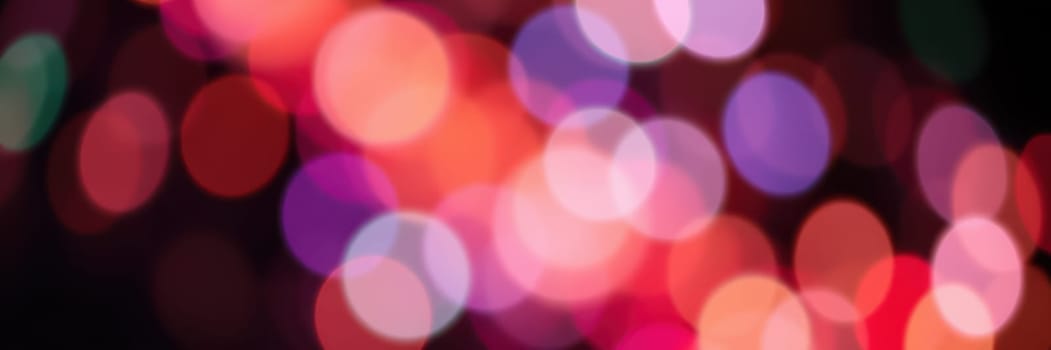 Vibrant bokeh lights in shades of red, purple, and blue illuminate a festive setting, enhancing the celebratory mood of a city event at night.
