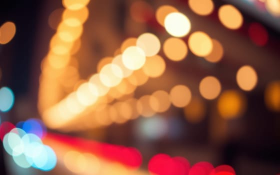Bright bokeh lights illuminate a bustling urban street at night. The colorful orbs and blurred outlines create a cheerful, inviting ambiance for pedestrians.