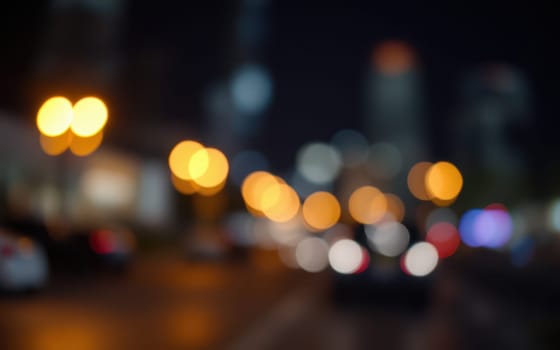 A bustling city street at night filled with blurred lights from street lamps and vehicle headlights creates a dynamic atmosphere. The scene captures the essence of urban nightlife.