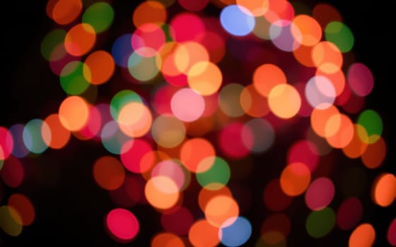 Bright, colorful bokeh lights twinkle in various hues, illuminating the dark surroundings. This festive display enhances the joyful ambiance of the urban night celebration.