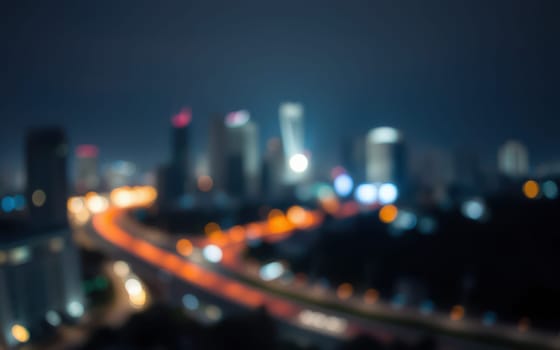 Bright lights from skyscrapers create a vibrant view of the city at night. Traffic flows along the road, adding to the lively atmosphere of the urban landscape.
