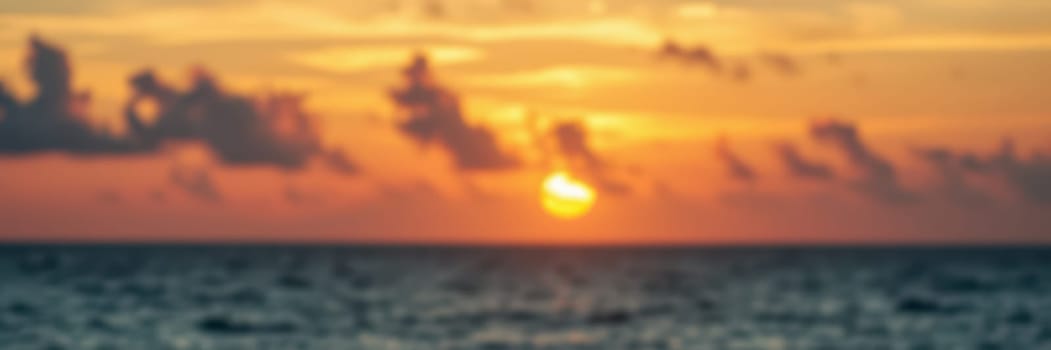 A breathtaking sunset unfolds over the ocean, featuring brilliant hues of orange and yellow blending into the sky. Gentle waves reflect the fading light during the evening.