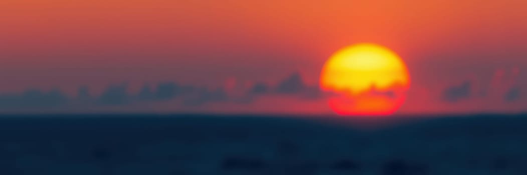 A spectacular sunset unfolds as the sun descends toward the horizon, casting warm orange and yellow hues across the sky and silhouetting the distant landscape.