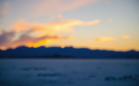 A stunning sunset paints the sky with vibrant hues while the silhouette of mountains frames the ocean below. The soft focus adds a serene quality to the scene captured just before nightfall.