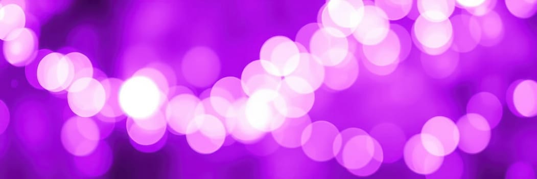 Soft purple bokeh lights illuminate a festive atmosphere in an outdoor urban location. The blurred lights create a whimsical effect, enhancing the evening ambiance.