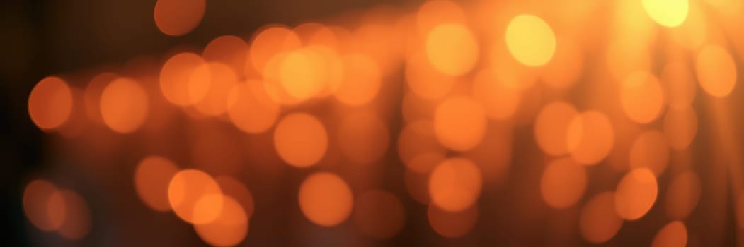 A swirl of soft orange bokeh lights fills a dim space, creating a warm atmosphere for an evening gathering. The blurred lights evoke a sense of coziness and celebration.