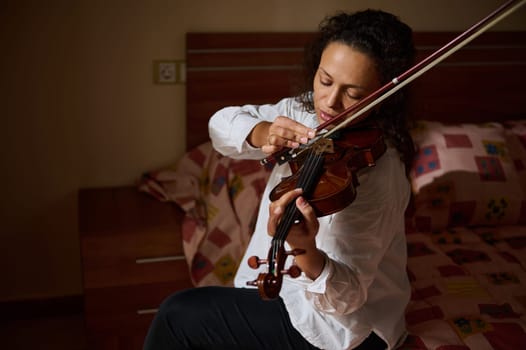 A woman engrossed in playing the violin in her bedroom, fostering a serene and artistic atmosphere.