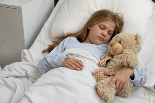 A young girl is peacefully sleeping in her cozy bed, clutching her teddy bear in a comforting medical environment