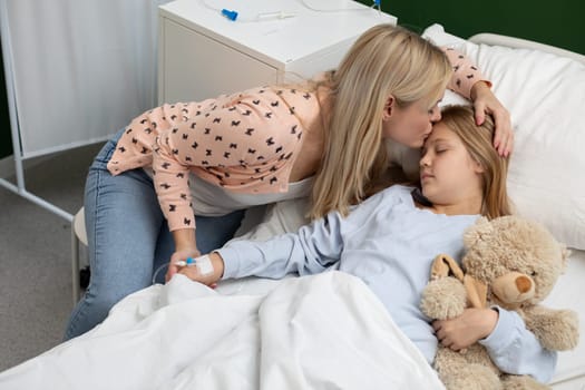 A mother kisses her daughter in the hospital, offering comfort and reassurance during this difficult time