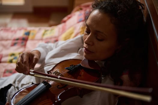 A woman peacefully rests with a violin, exuding calmness and musical passion. Her serene expression and the warm setting create a sense of relaxation and artistic contemplation.