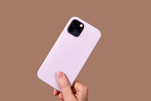 Hand holding sleek purple smartphone featuring multiple camera lenses against a rich brown background, highlighting modern mobile technology design elements Mocha Mousse color of 2025 year