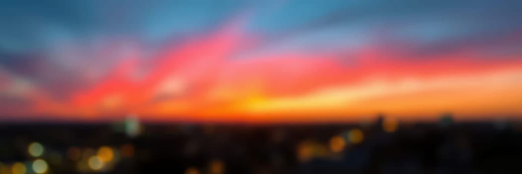 A stunning display of oranges, pinks, and blues fills the sky above a city skyline as daylight fades into twilight. Blurred city lights add to the ambiance of the evening.