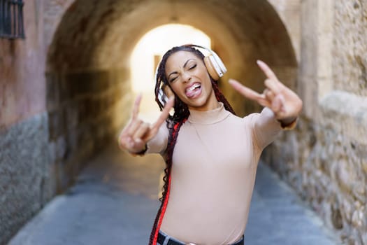 A cheerful and vibrant young woman expresses pure joy while wearing headphones in a bustling urban archway, perfectly showcasing her youthful energy, trendy style, and confident demeanor