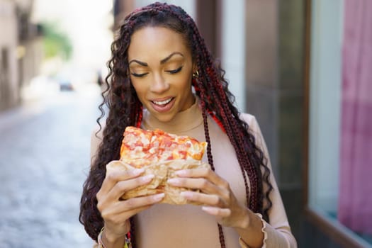 A joyful woman, full of energy and happiness, indulges in a delicious slice of pizza as she strolls down a charming city street, perfectly showcasing the delightful bliss of enjoying street food