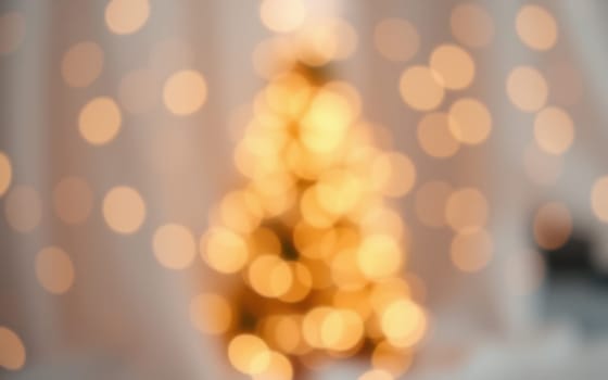 A beautifully decorated Christmas tree glows with soft warm lights, filling the cozy living room with a festive spirit. The blurred background adds a dreamy effect to the scene.