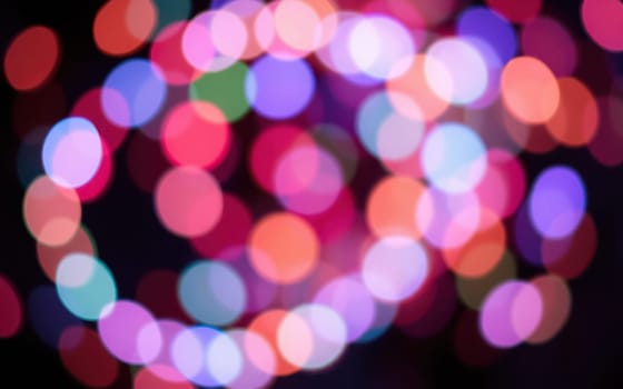 Brightly colored bokeh lights illuminate the night sky, creating a lively ambiance for evening festivities in the park. People enjoy the vibrant atmosphere and celebrate together.