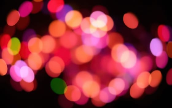 Soft, blurred lights in various colors illuminate the surroundings, creating a joyful ambiance typical of nighttime festivities in an urban area.