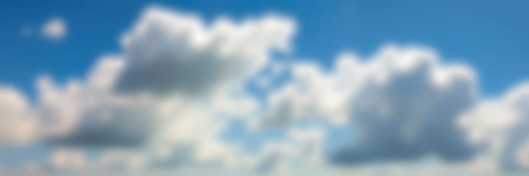 Fluffy white clouds float gently in a clear blue sky, casting shadows and providing a peaceful backdrop during a calm afternoon. The scene evokes a sense of serenity.