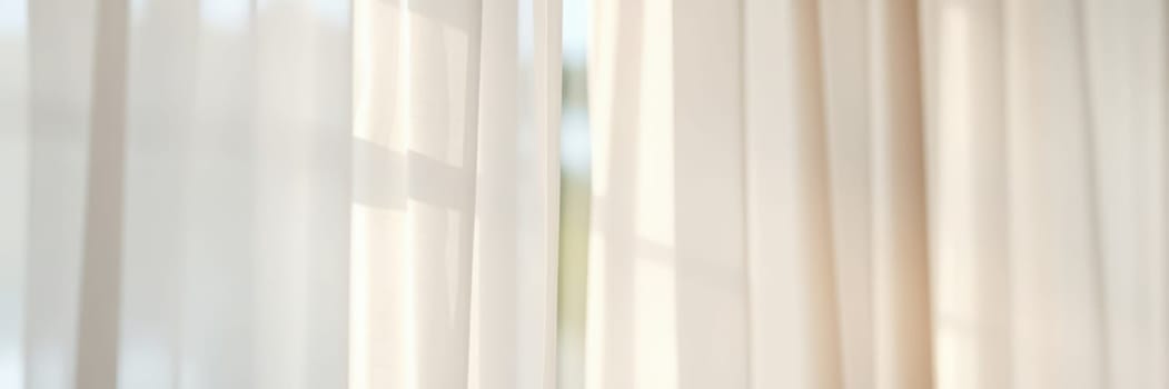 Sunlight softly pours into a bright room, creating a peaceful atmosphere as it passes through sheer white curtains, enhancing the lightness of the space.