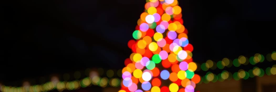 A dazzling Christmas tree glows with vibrant lights of various colors against a dark evening backdrop, creating a festive atmosphere for holiday gatherings.