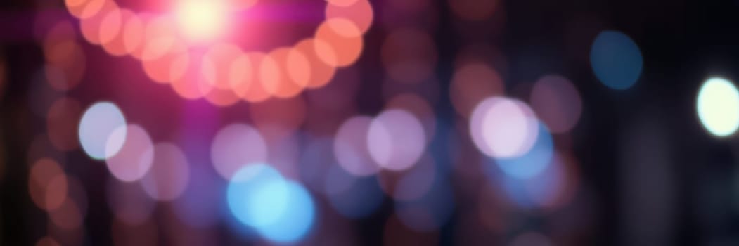 Bright, blurred lights illuminate the night sky, creating a festive mood in the city square. People gather to enjoy music and entertainment during the lively celebration.
