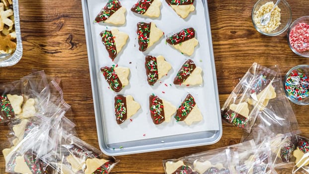 Flat lay. Carefully packaging Christmas cutout cookies, half-dipped in chocolate, sprinkled with crushed nuts, and presented in clear cellophane wrapping.